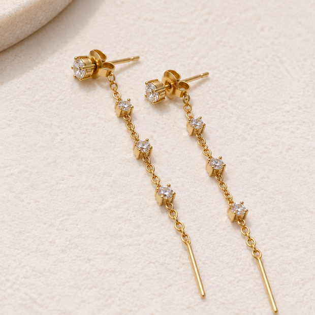 Boucles d’oreilles dorées pendantes Éclat avec pierres transparentes et chaîne au fermoir arrière