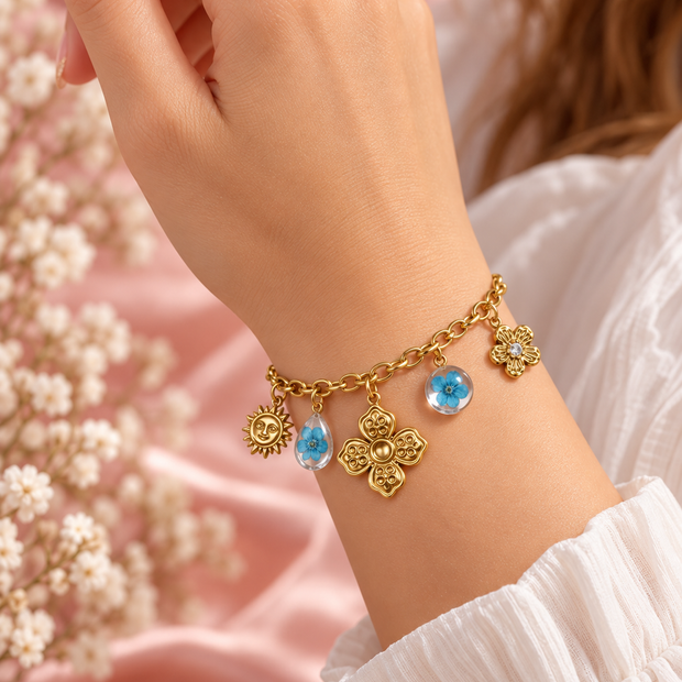 Bracelet Flora doré porté au poignet, breloques fleurs et soleil et deux ornements floraux bleus – Secret de Rose bijoux