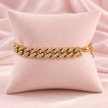 Bracelet maille gourmette doré orné de strass transparents sur un coussin rose pâle