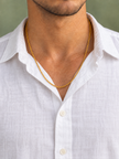 Chaîne simple dorée portée par un homme en chemise blanche boutonnée sur fond vert sauge