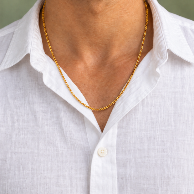 Chaîne simple dorée portée par un homme en chemise blanche boutonnée sur fond vert sauge