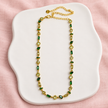 Collier Prisme en acier et strass – Doré – Vert sur support blanc et fond rose