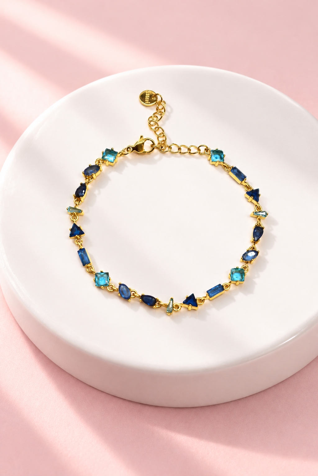 Gourmette Prisme en acier inoxydable et strass – Doré – Bleu sur support blanc et fond rose